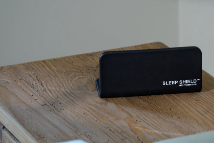 Phone under The Sleep Shield EMF-blocking cover beside bed